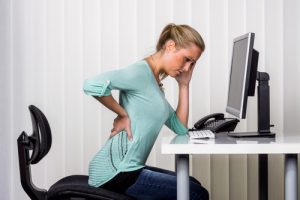 workers' compensation lawyer Memphis TN with a woman holding her back in pain sitting at a desk